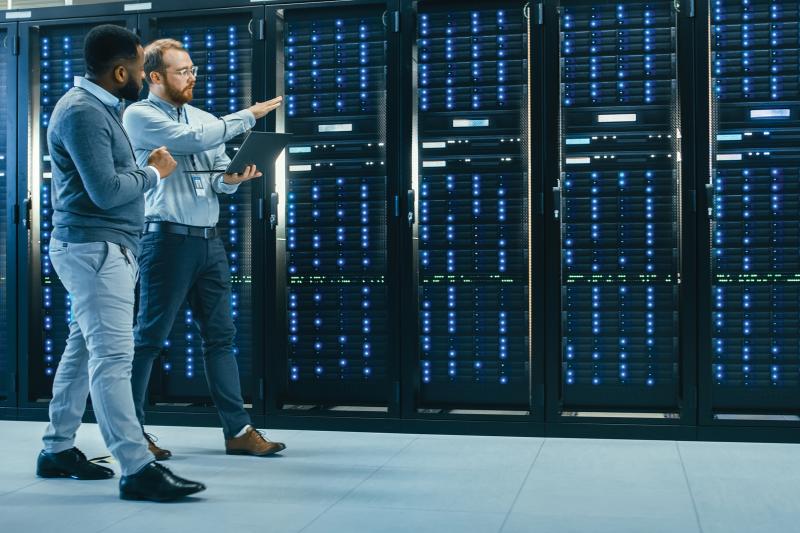 2 men walking along server racks and talking 