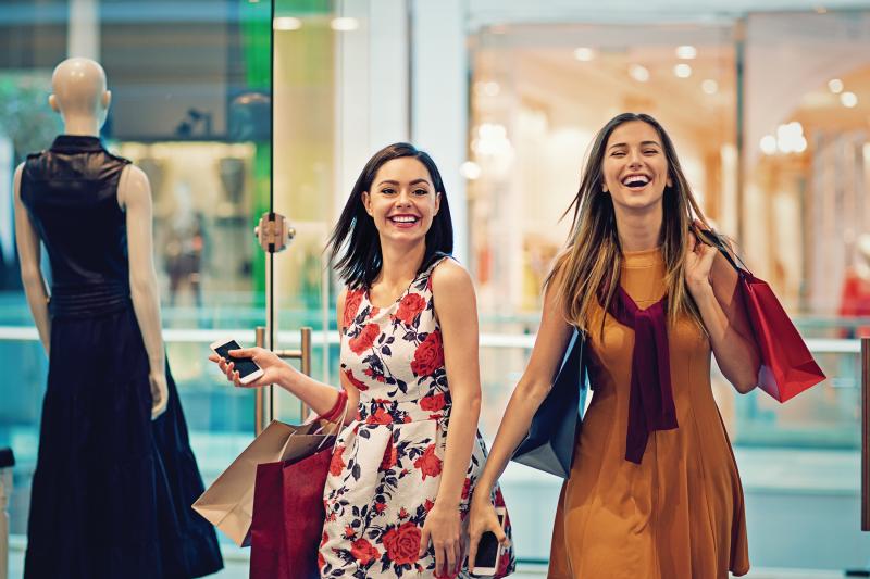 two happy women with shopping bags entering a store