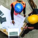 architect builders wearing helmets, looking at a laptop screen