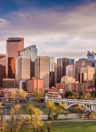 Skyline at sunset, skyscrapers in golden light, bridge and river in front.