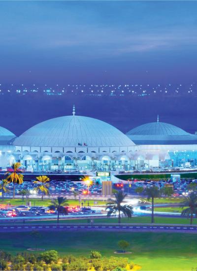 Exterior of airport in evening, white building and palm trees in front.