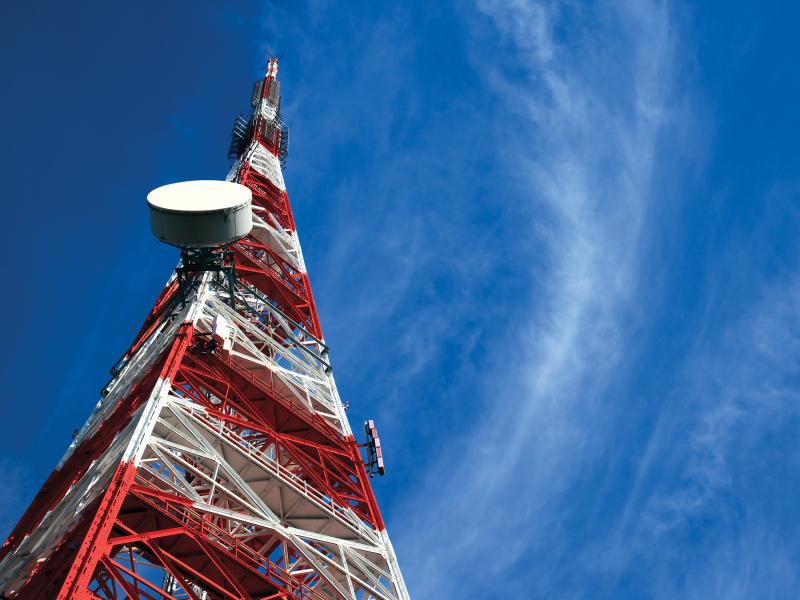 Red and white telecommunications tower in a blue sky